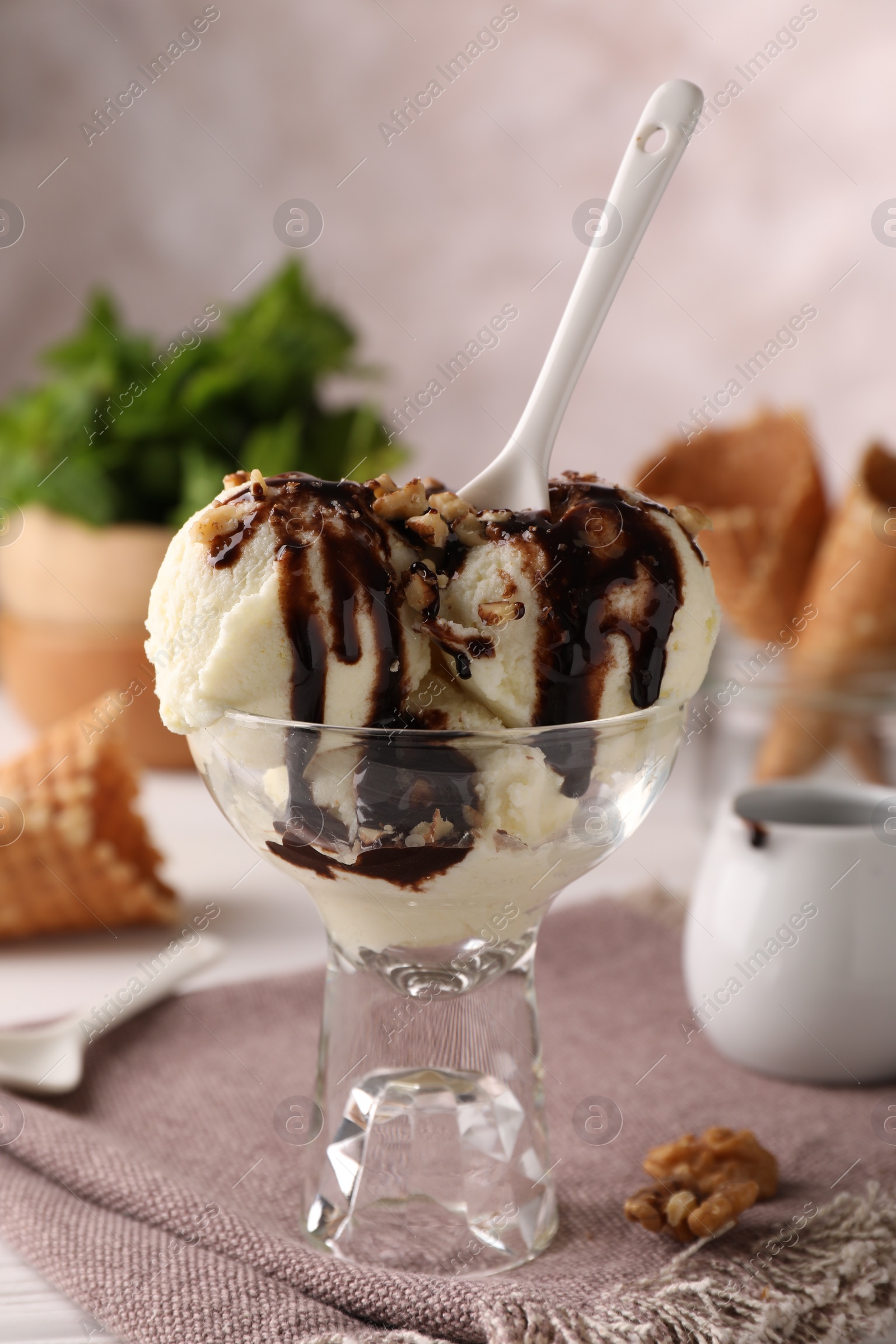 Photo of Tasty ice cream with chocolate topping and nuts in glass dessert bowl on table, closeup