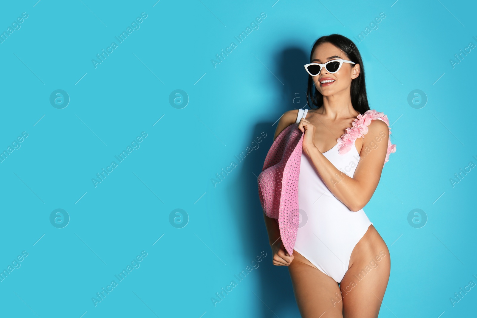 Photo of Beautiful young woman in white bikini with hat on light blue background. Space for text