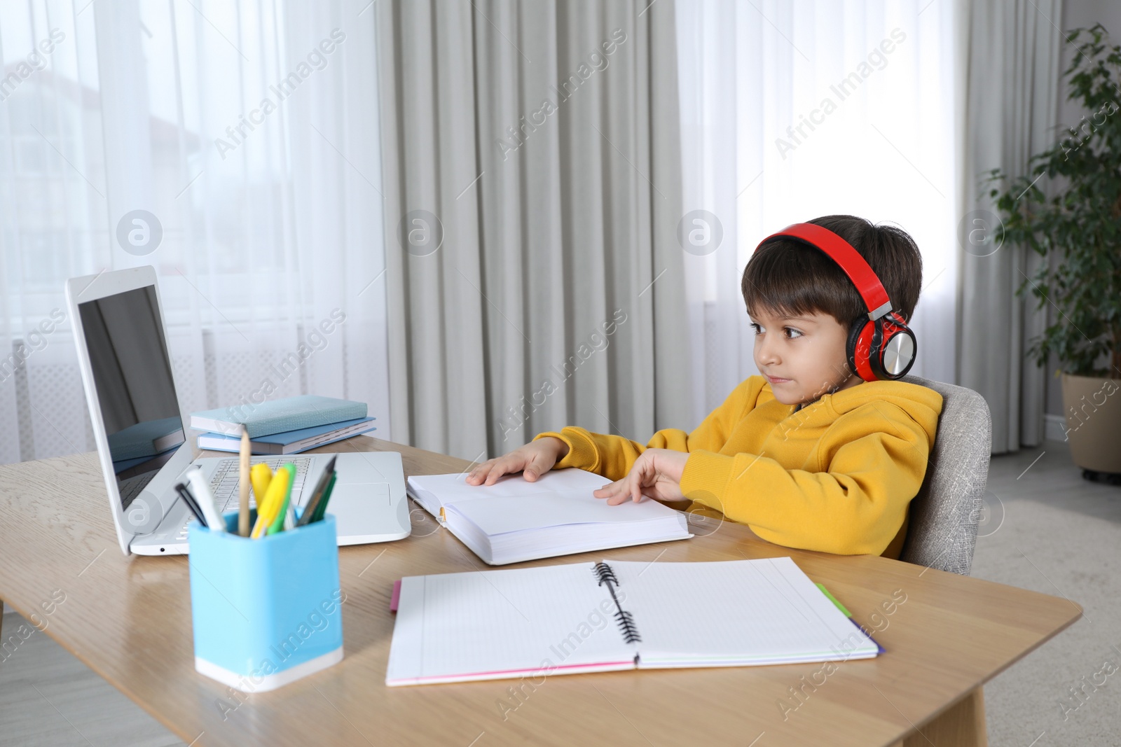 Photo of Cute little boy with modern laptop studying online at home. E-learning