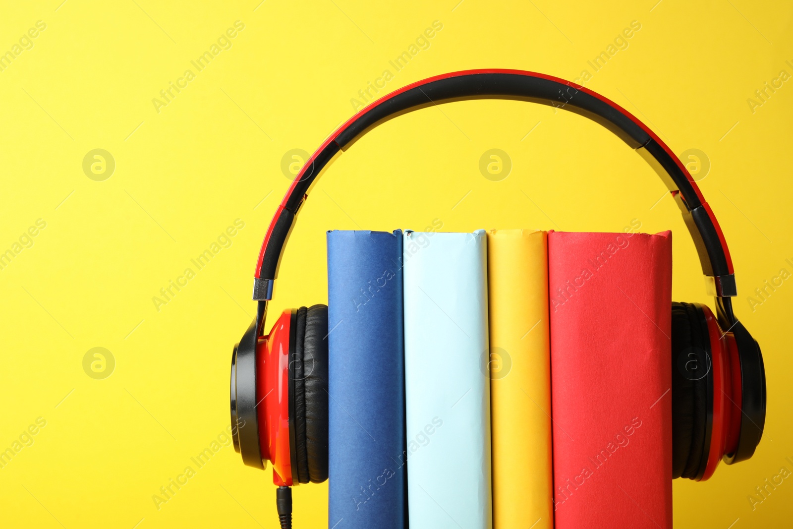 Photo of Books with modern headphones on yellow background. Space for text