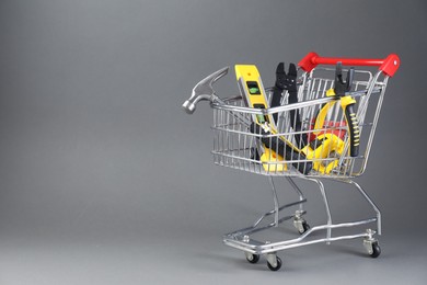 Photo of Small shopping cart with set of construction tools on grey background. Space for text