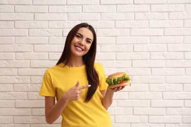 Photo of Young woman with tasty burger near brick wall. Space for text
