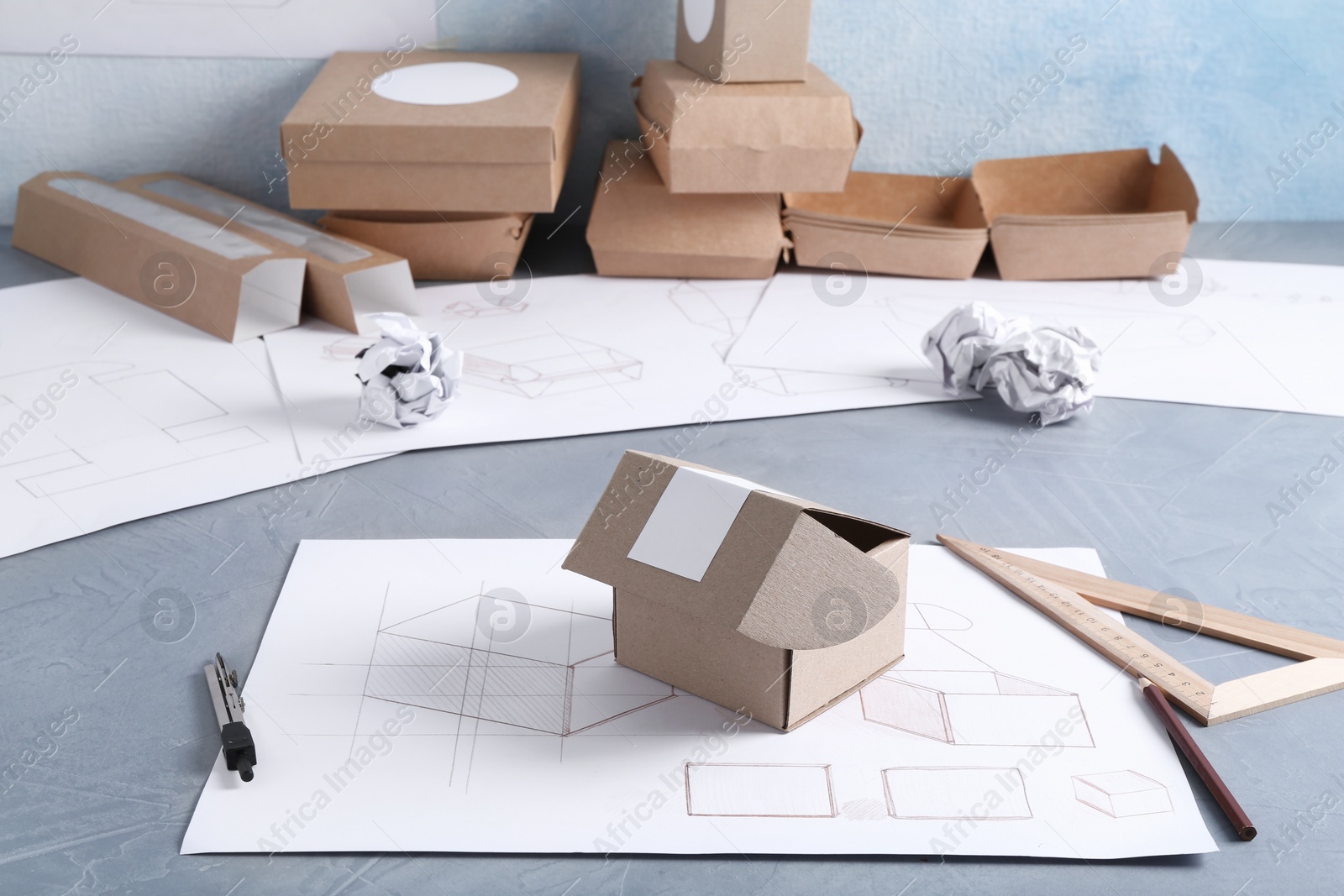 Photo of Creating packaging design. Drawings, boxes and stationery on blue textured table, closeup