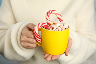 Photo of Woman holding cup of tasty cocoa with marshmallows and Christmas candy canes, closeup