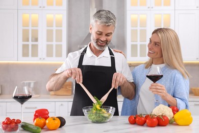 Happy affectionate couple cooking together at white table in kitchen