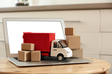 Photo of Laptop and truck model with boxes on table indoors. Courier service