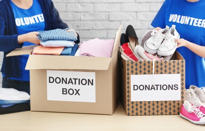 Photo of Female volunteers collecting clothes and shoes into donation boxes indoors