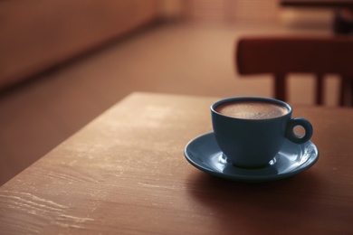 Photo of Cup of fresh aromatic coffee on table against blurred background. Space for text