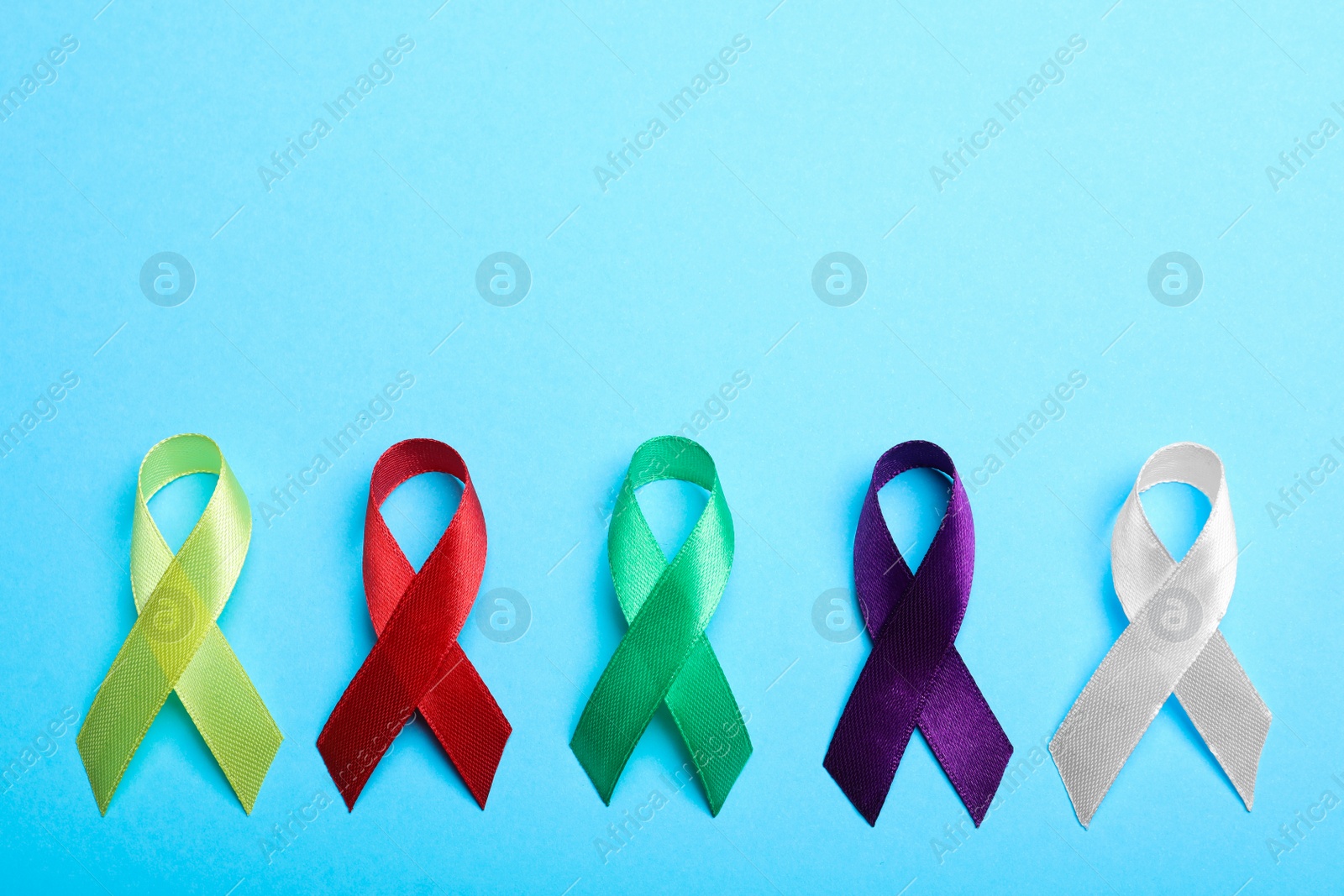 Photo of Colorful ribbons on light blue background, flat lay with space for text. World Cancer Day