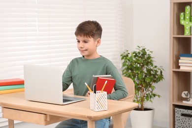 Boy with books using laptop at desk in room. Home workplace