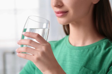 Photo of Healthy habit. Woman drinking fresh water from glass indoors, closeup