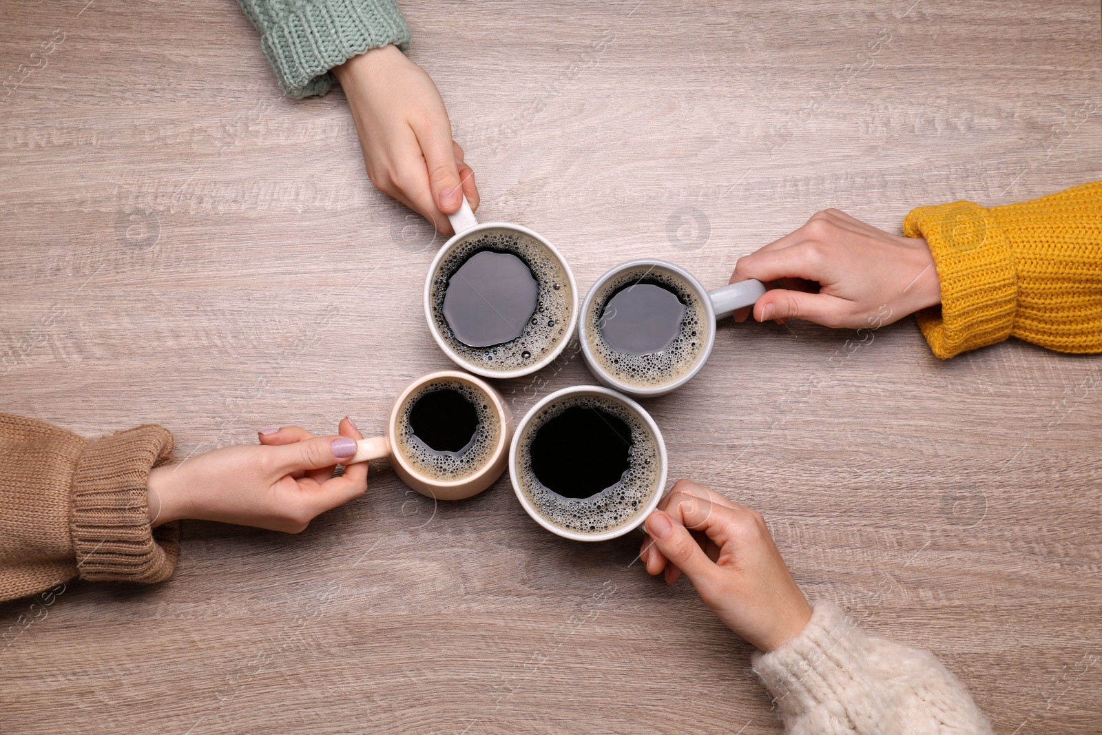 Photo of Women with cups of coffee at wooden table, top view