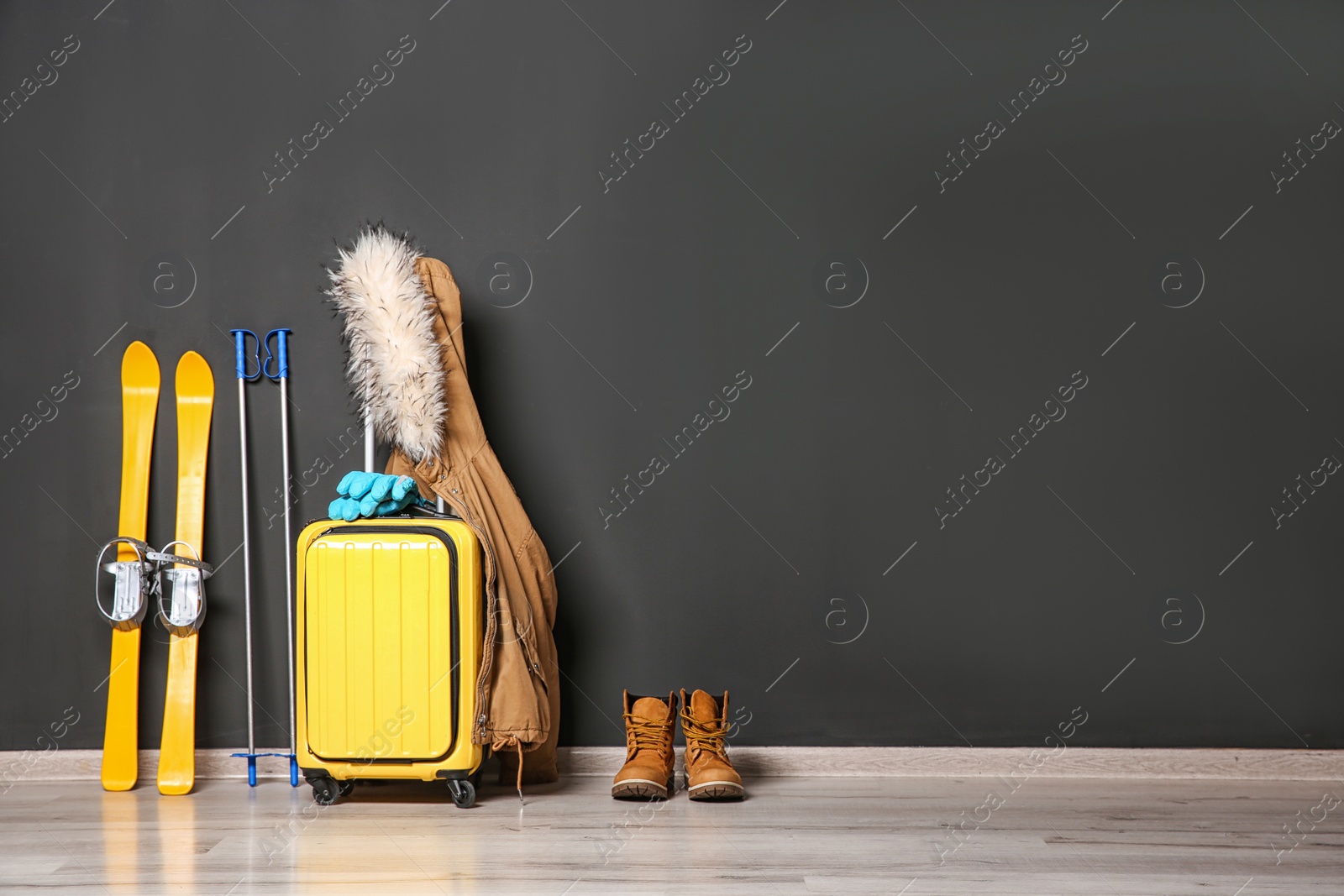 Photo of Suitcase, jacket and skis on floor against black wall, space for text. Winter vacation