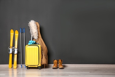 Photo of Suitcase, jacket and skis on floor against black wall, space for text. Winter vacation