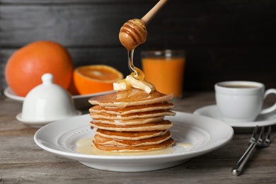 Photo of Pouring honey onto delicious pancakes with butter on table