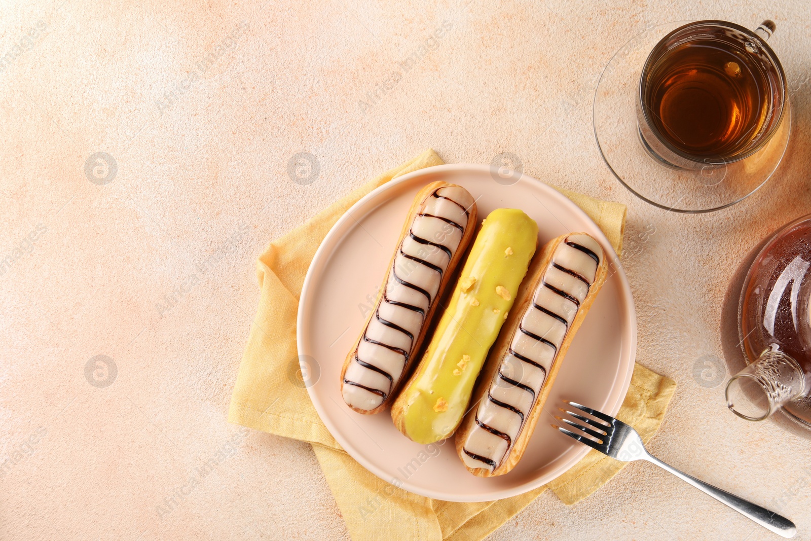 Photo of Different tasty glazed eclairs and tea served on color textured table, flat lay. Space for text