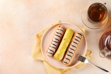 Different tasty glazed eclairs and tea served on color textured table, flat lay. Space for text