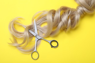 Professional hairdresser scissors and hair strands on yellow background, flat lay. Haircut tool