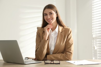 Portrait of beautiful young businesswoman with laptop at table in office