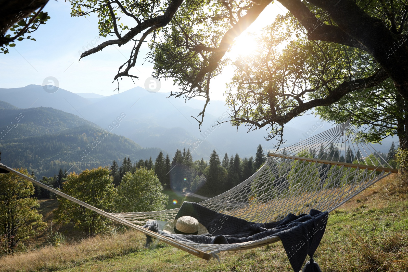 Photo of Comfortable net hammock with hat and blanket in mountains on sunny day