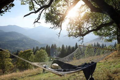 Comfortable net hammock with hat and blanket in mountains on sunny day