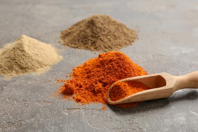 Photo of Different types of powdered pepper and wooden scoop on table