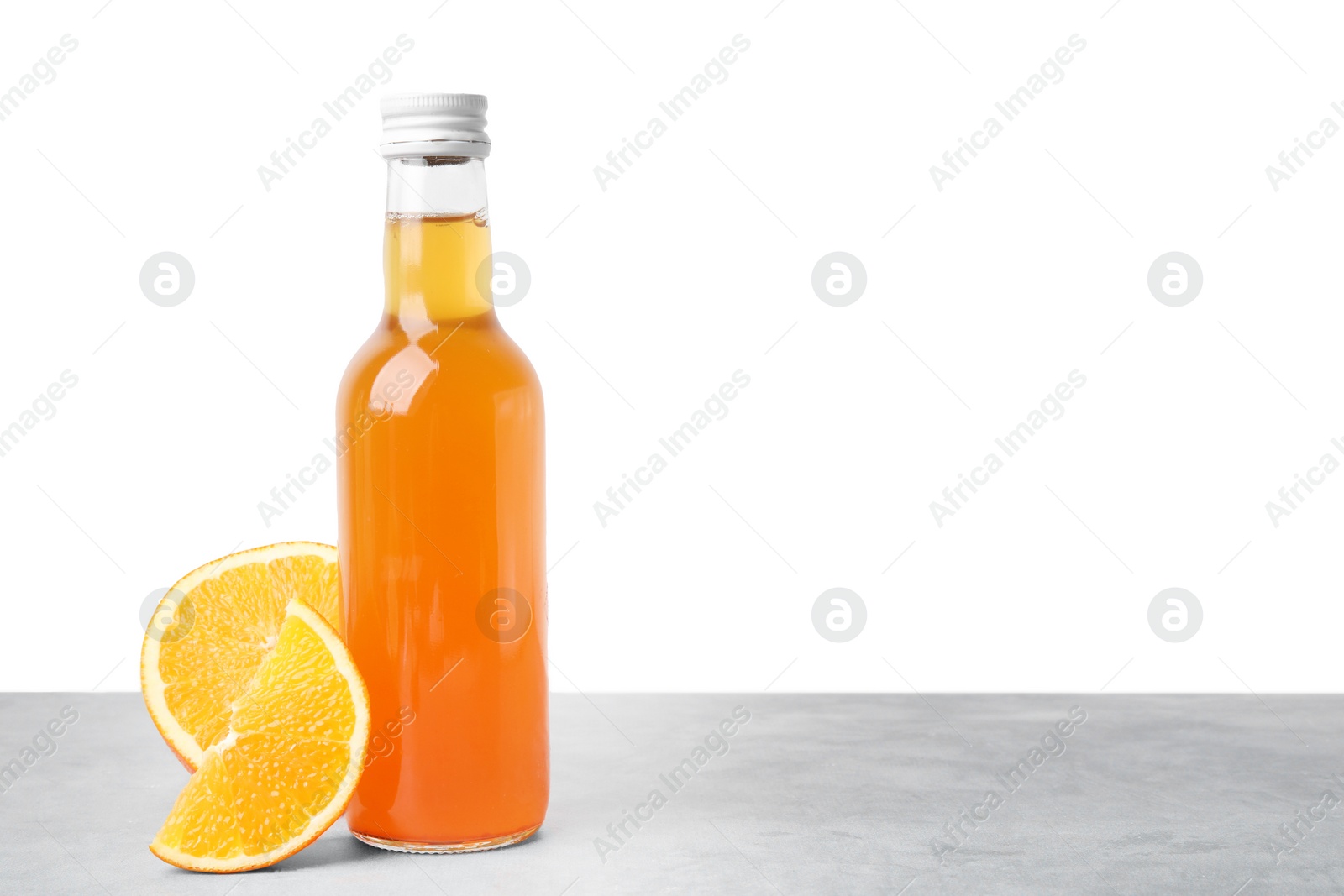 Photo of Delicious kombucha in glass bottle and orange on grey table against white background, space for text