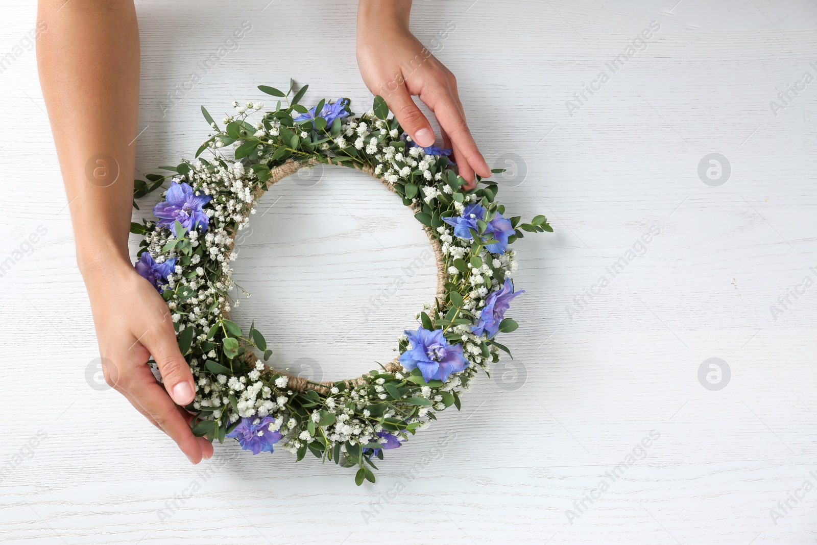 Photo of Woman making flower wreath at white wooden table, closeup. Space for text