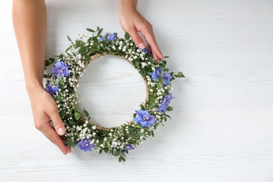 Woman making flower wreath at white wooden table, closeup. Space for text