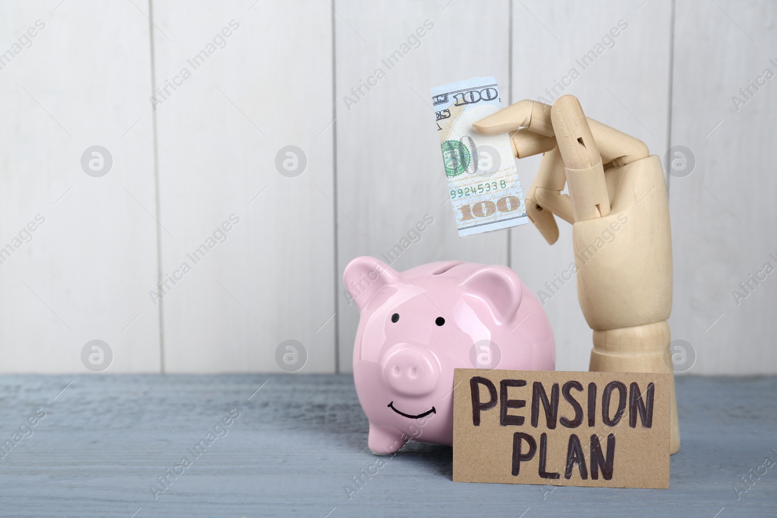 Photo of Card with phrase Pension Plan, mannequin hand holding dollar banknote and piggy bank on light blue wooden table, space for text. Retirement concept