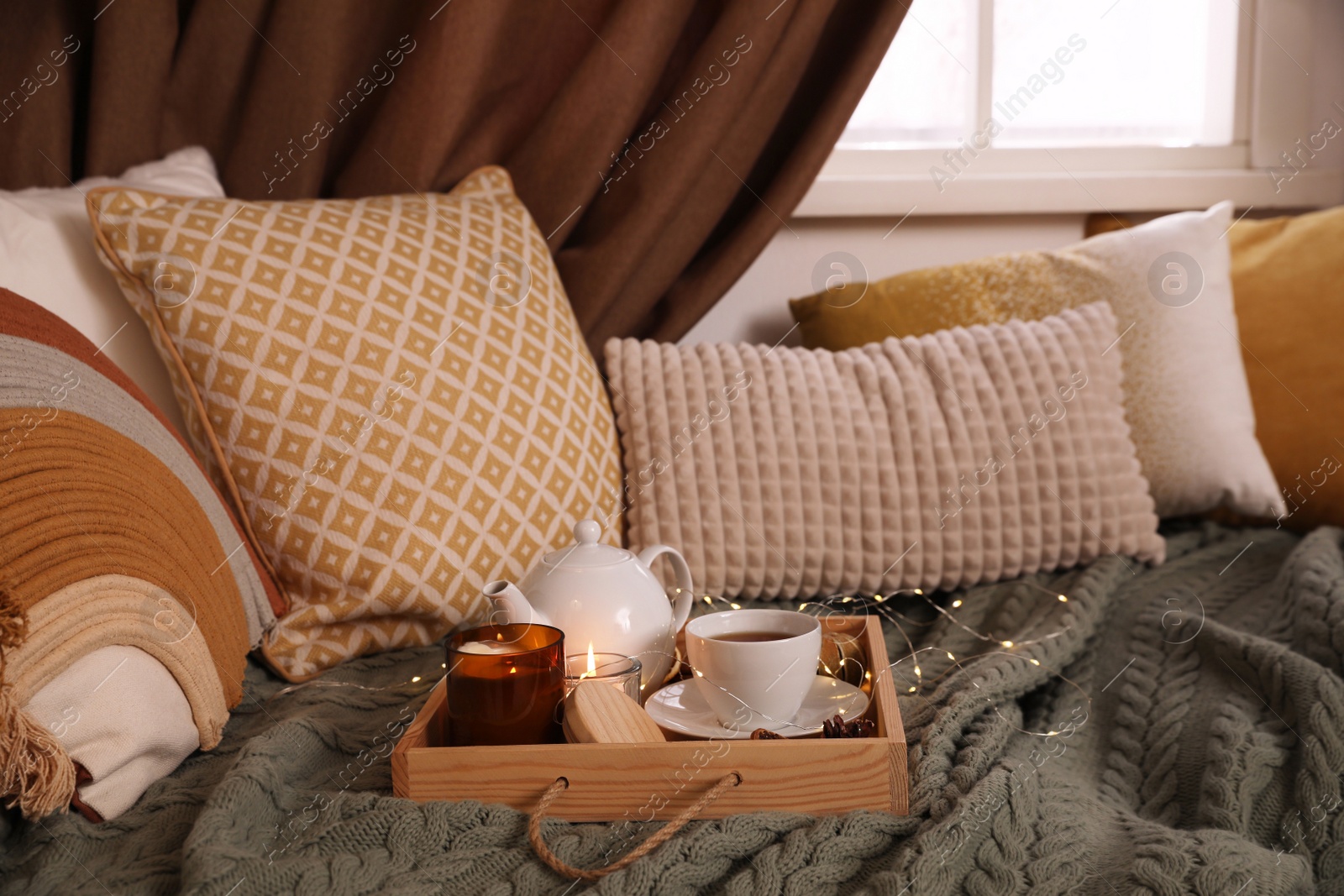 Photo of Comfortable lounge area with knitted blanket and soft pillows near window in room