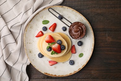 Delicious pancakes served with berries and chocolate spread on wooden table, top view