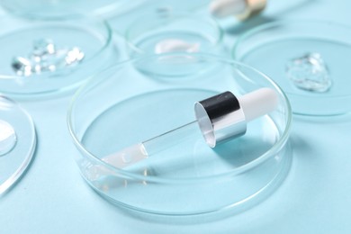 Petri dish and pipette with cosmetic serum on light blue background, closeup