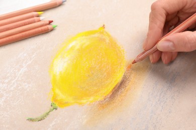 Photo of Woman drawing lemon on paper with pastel pencil at table, closeup