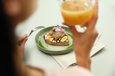 Photo of Woman with glass of beer and tasty fish sandwich at light table