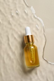 Bottle of cosmetic oil in water on beige background, top view.