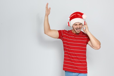 Young man in Santa hat listening to Christmas music on color background