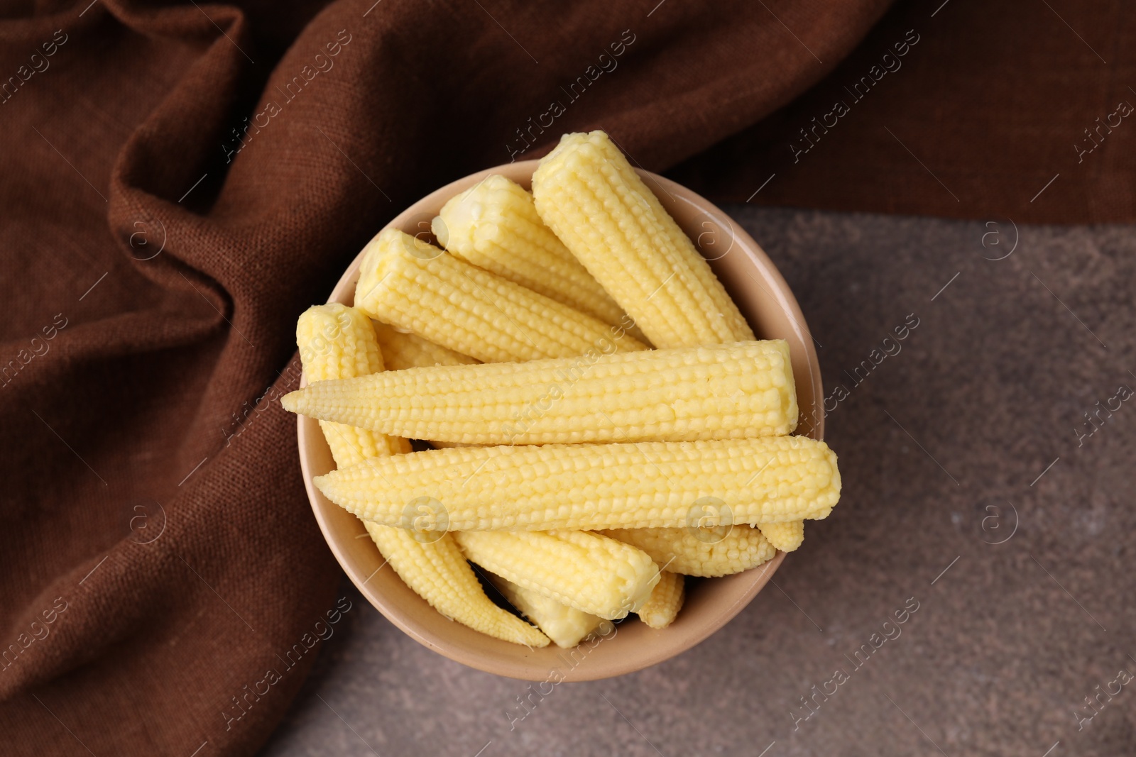 Photo of Tasty fresh yellow baby corns in bowl on brown table, top view