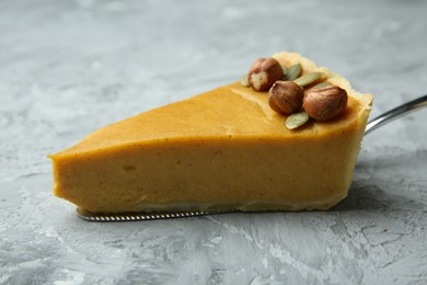 Photo of Cake server with piece of delicious pie with hazelnuts and pumpkin seeds on grey textured table, closeup