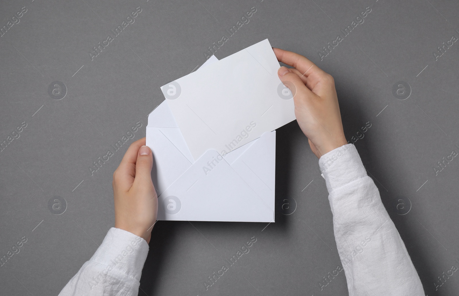 Photo of Woman taking card out of letter envelope at grey table, top view. Space for text