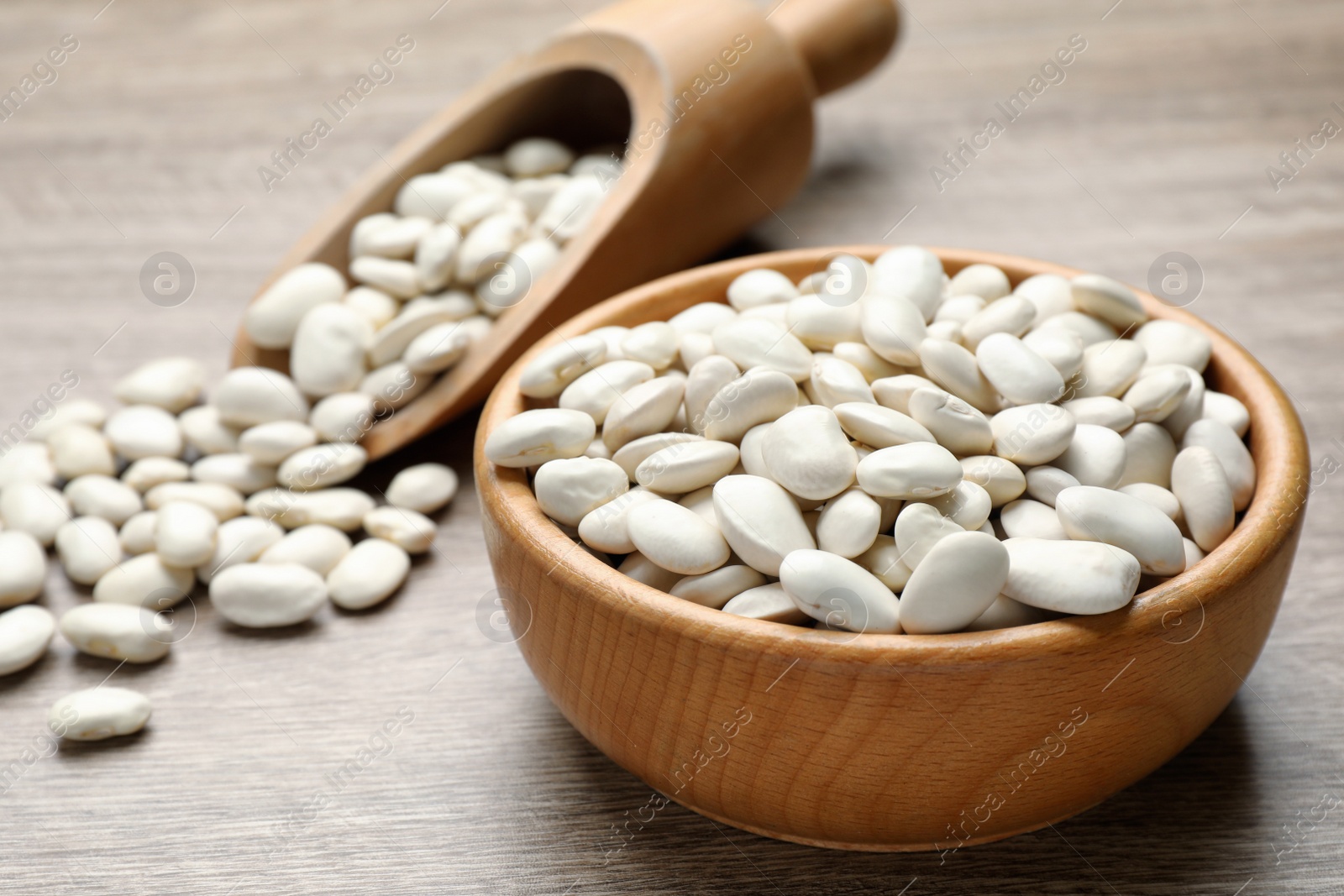 Photo of Raw white beans, bowl and scoop on wooden table, closeup