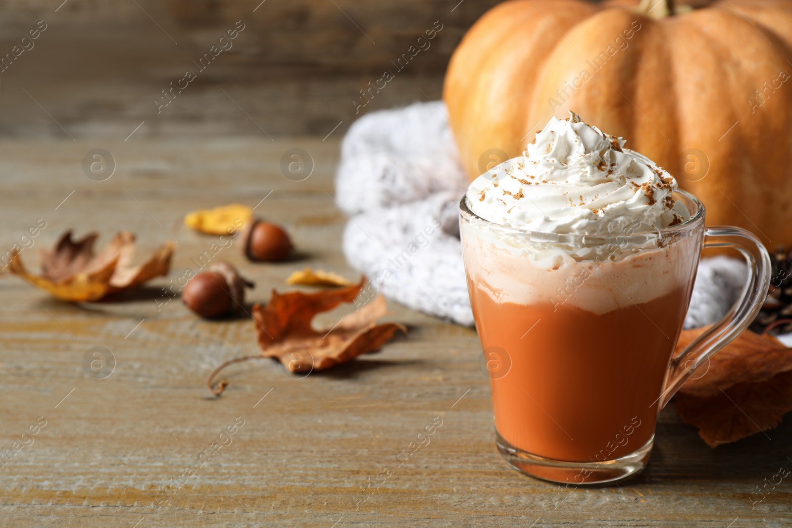 Photo of Pumpkin spice latte with whipped cream in glass cup on wooden table. Space for text