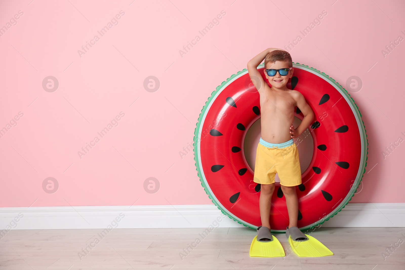 Photo of Cute little boy with inflatable ring wearing flippers near color wall