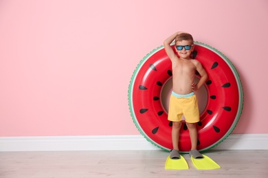 Cute little boy with inflatable ring wearing flippers near color wall