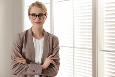 Young businesswoman standing near window in office. Space for text