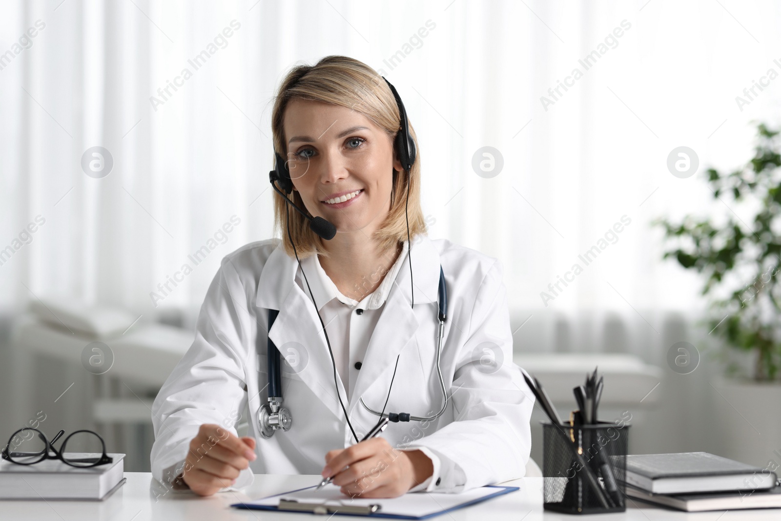 Photo of Smiling doctor in headphones having online consultation at table indoors