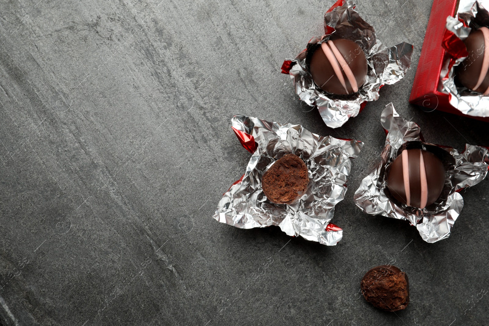 Photo of Many different delicious chocolate truffles with wrappers on grey table, flat lay. Space for text