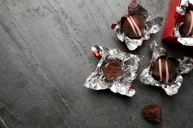 Many different delicious chocolate truffles with wrappers on grey table, flat lay. Space for text