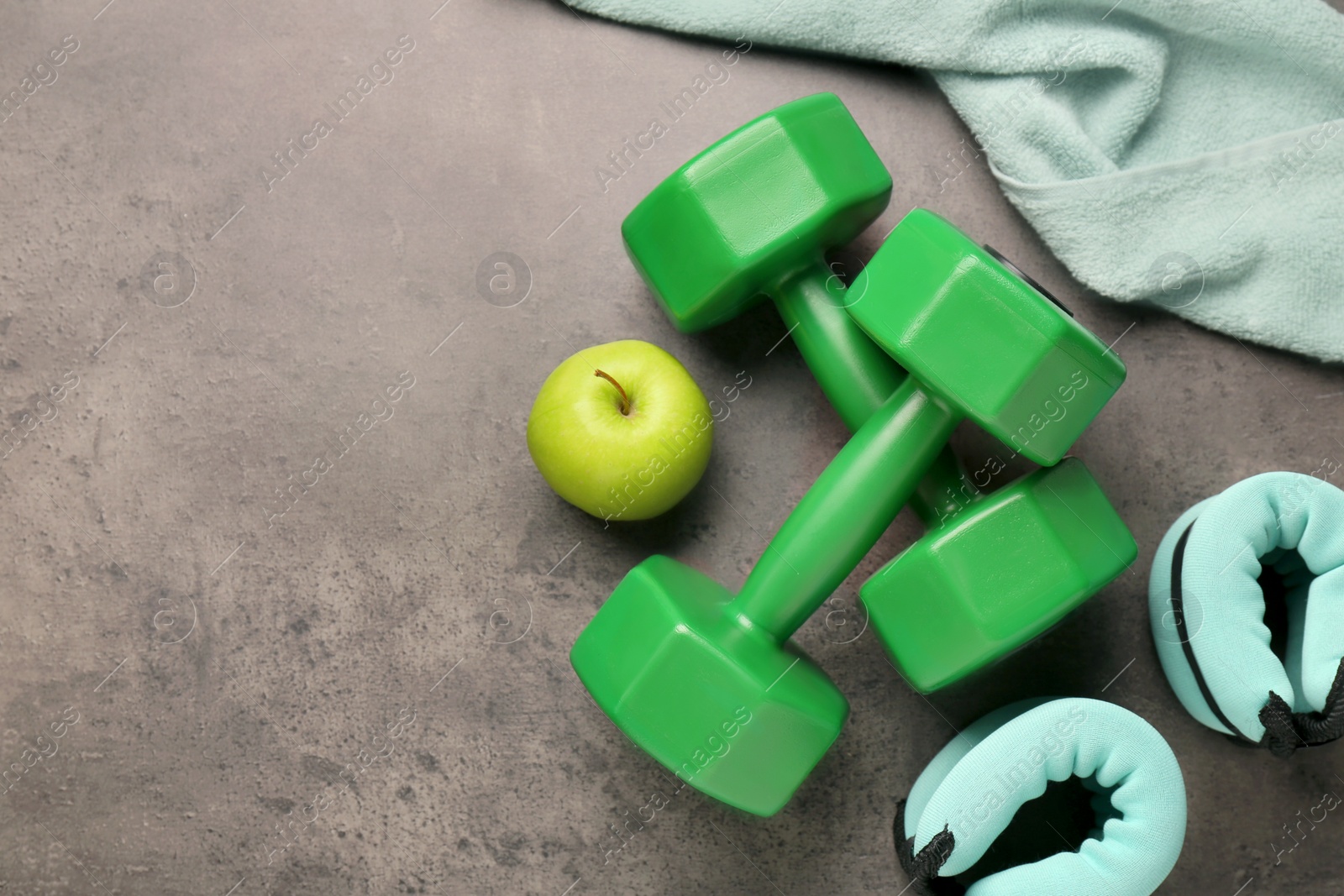 Photo of Dumbbells, apple, weights and towel on brown textured table, flat lay. Space for text