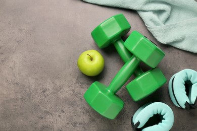 Photo of Dumbbells, apple, weights and towel on brown textured table, flat lay. Space for text